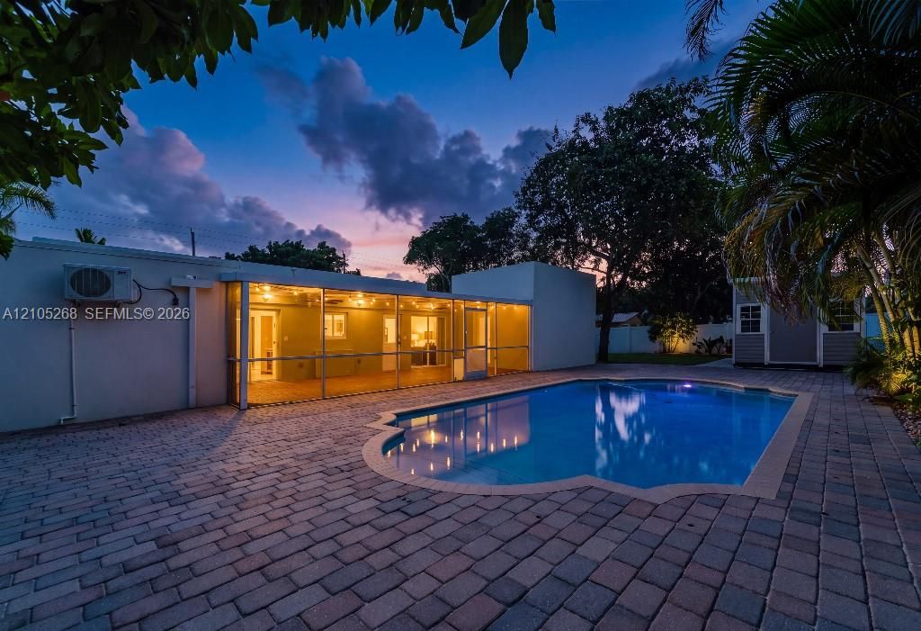 Paved patio surrounding a freeform pool, screened patio with overhead lighting, and a detached structure
