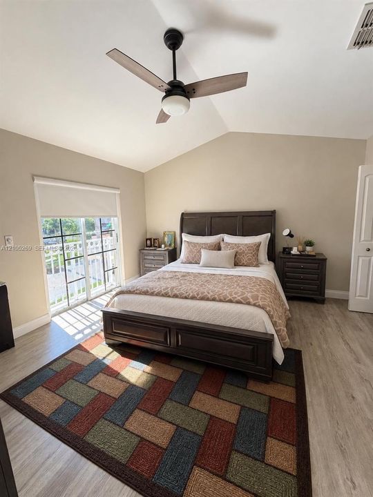 Vaulted ceiling with an attached ceiling fan, wood-finish flooring, and a sliding glass door leading to a balcony