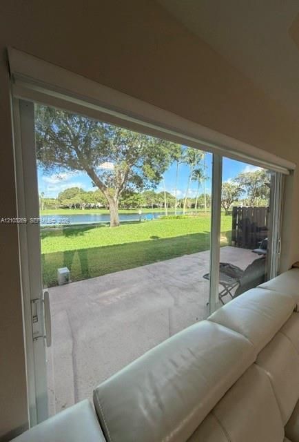Sliding glass doors opening to a concrete patio, featuring a manicured lawn and a body of water in the background