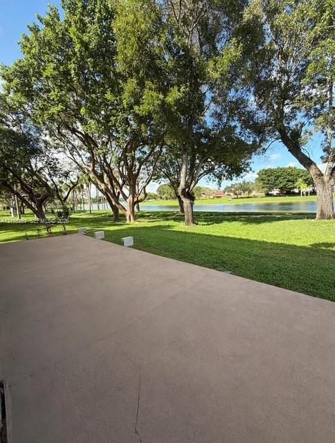 Paved outdoor area featuring a manicured lawn and mature trees with a visible body of water beyond