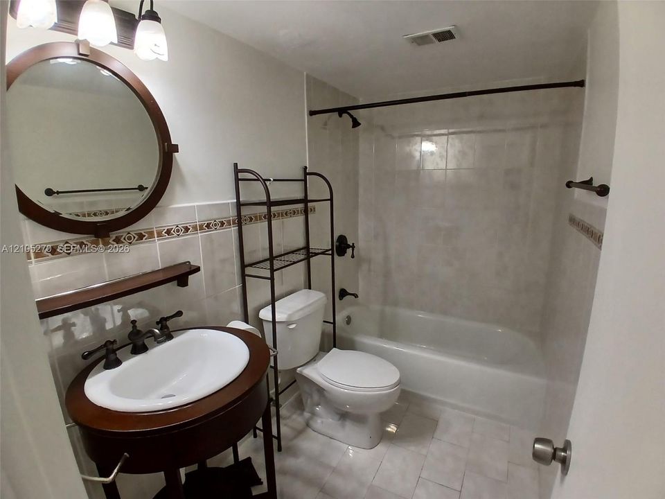 Tile flooring and shower surround, wall-mounted vanity mirror, and dark bronze fixtures