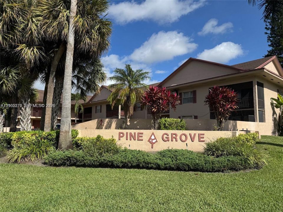 Prominent property signage, mature palm trees, established landscaping, screened outdoor living spaces, and a neutral-toned building exterior