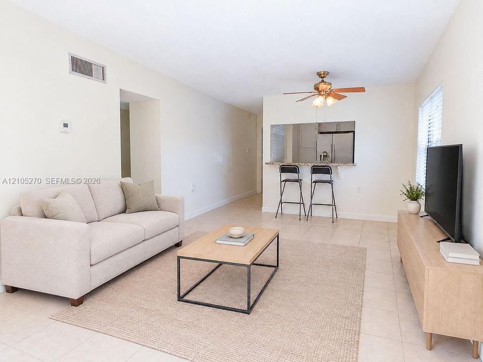 Tiled flooring with an open concept layout, kitchen pass-through, ceiling fan, and stainless steel refrigerator