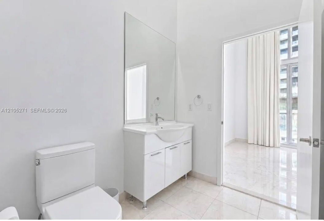 Bathroom featuring a white vanity cabinet with a integrated sink, polished chrome faucet, full-height wall mirror, and large-format tile flooring