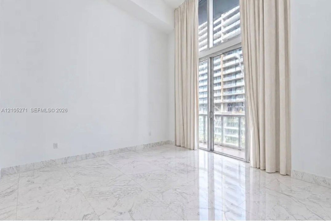 High-ceilinged room featuring polished stone-finish floor tiling, floor-to-ceiling glass paneling, and access to a balcony with glass railing