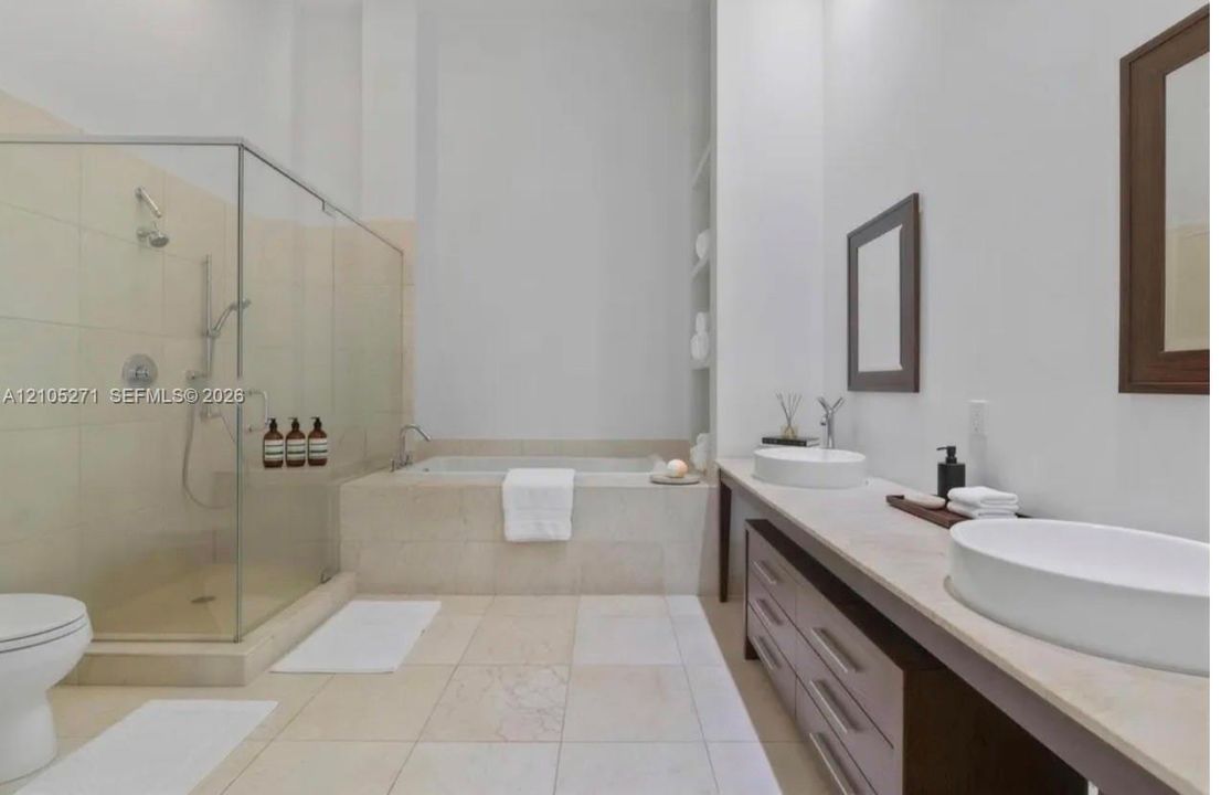 Bathroom featuring a glass-enclosed shower, built-in soaking tub, dual vessel sinks atop a stone vanity, and integrated wall shelving