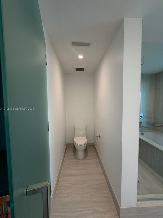 Enclosed water closet featuring a high-efficiency toilet, neutral stone-finish flooring, frosted glass door, and recessed lighting