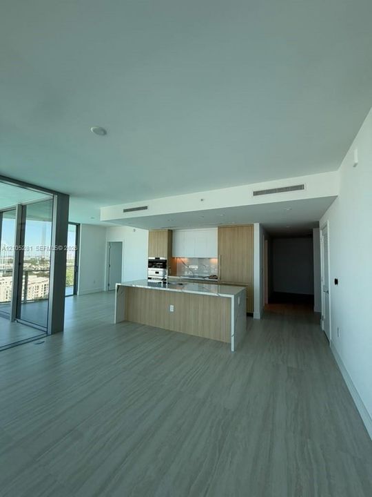 Kitchen featuring custom wood-finish cabinetry, a waterfall-edge stone countertop, built-in stainless steel oven, and expansive floor-to-ceiling glass sliding doors