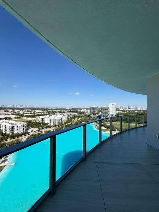 Curved balcony featuring large-format tile flooring and a glass panel railing with a dark metal frame