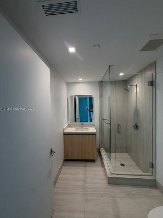Bathroom featuring wood-finish cabinetry, a rectangular undermount sink, a glass-enclosed shower with full-height tile surround, and large-format floor tiling