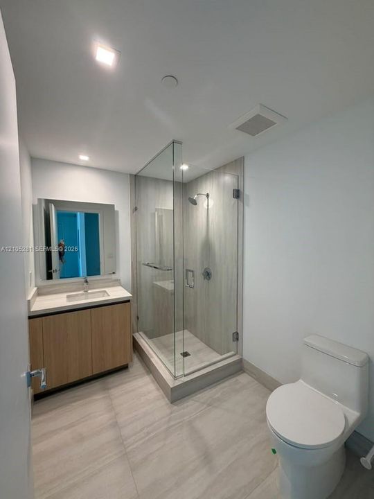 Bathroom featuring a wood-finish vanity with a rectangular undermount sink, a frameless glass-enclosed shower with floor-to-ceiling tile surround, and large-format neutral floor tile