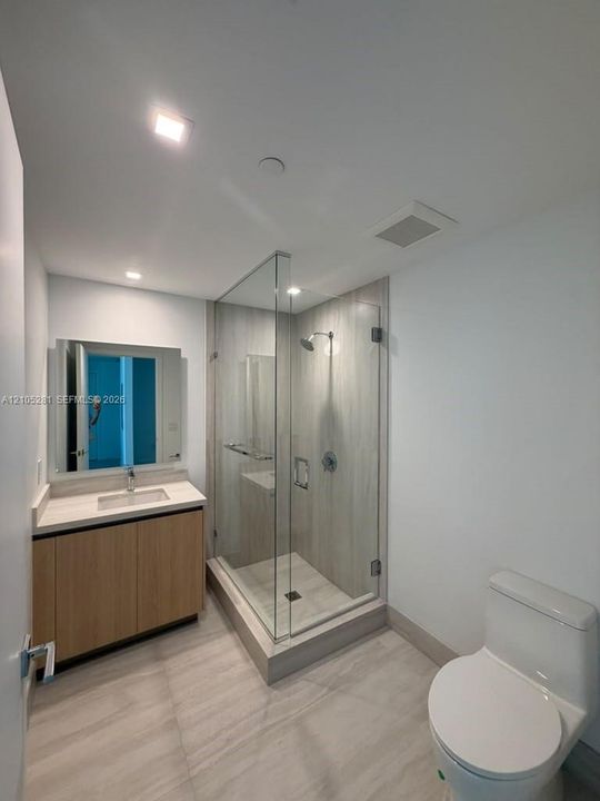 Bathroom featuring a wood-finish vanity with a stone countertop, an integrated rectangular sink, a glass-enclosed shower with large-format wall tile, and recessed lighting