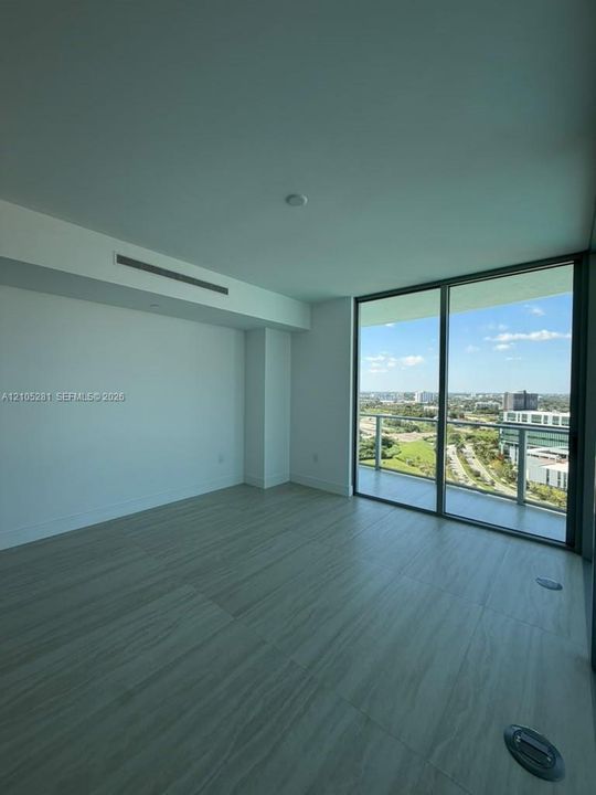 Floor-to-ceiling windows, wood-finish flooring, and access to a glass-railed balcony with a landscape backdrop