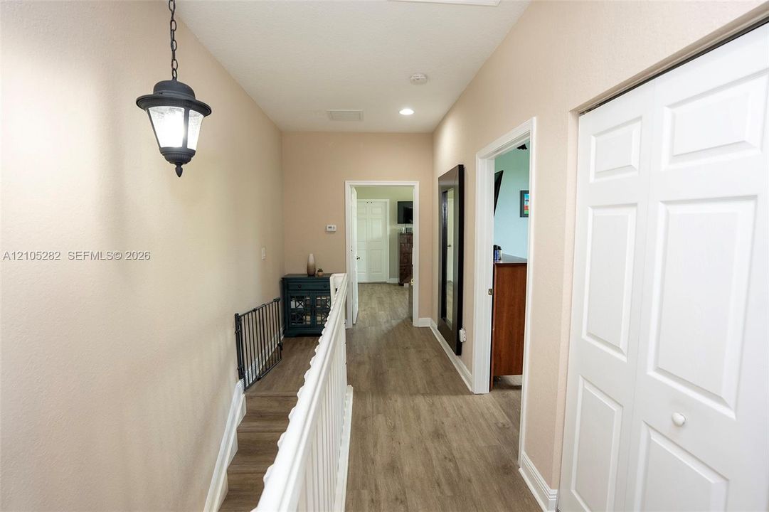 Hallway featuring wood-finish flooring, a hanging lantern-style light fixture, white wood-slat railing, and bifold closet doors