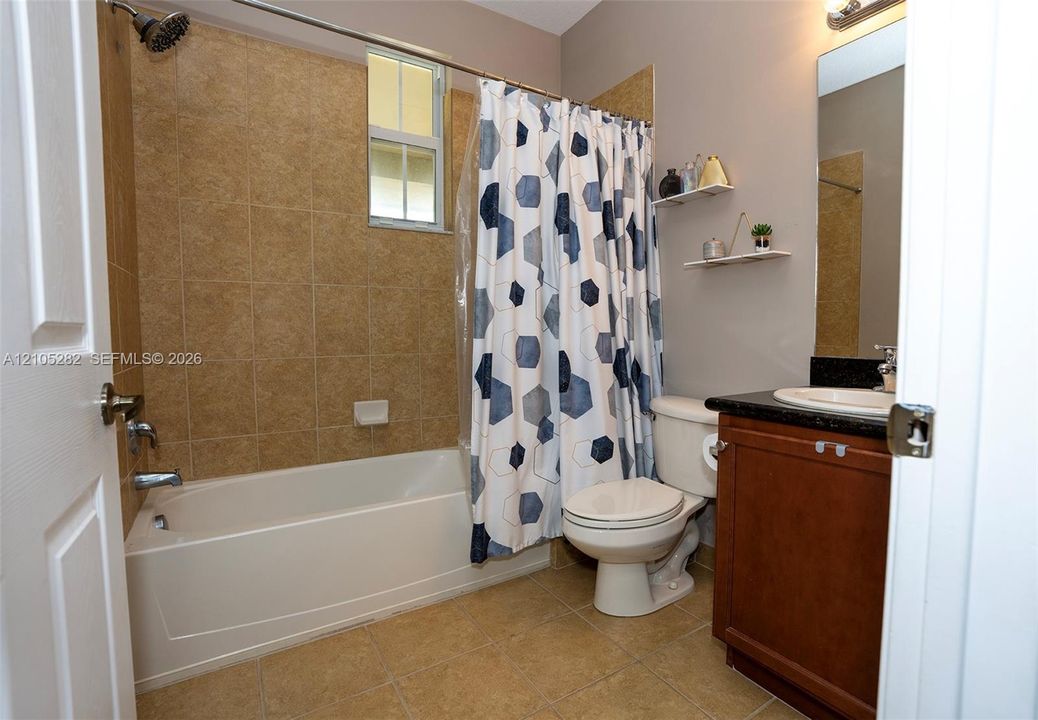 Bathroom featuring a tub-shower combination with floor-to-ceiling tile surround, dark-toned vanity with a contrasting solid surface countertop, inset sink, and built-in wall shelving
