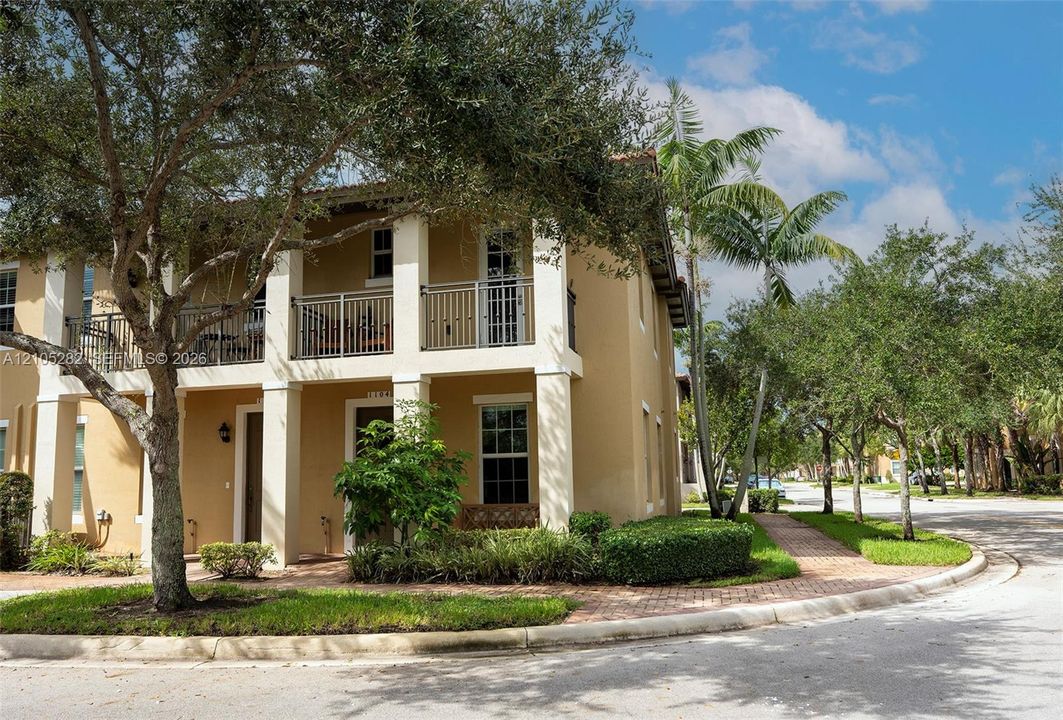 Two-story exterior featuring a stucco facade, covered ground-floor patio, second-level balcony with metal railings, and a paver walkway