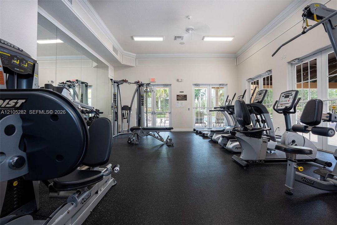 Fitness center featuring rubber flooring, floor-to-ceiling mirrored walls, crown molding, and dual glass-paned double doors