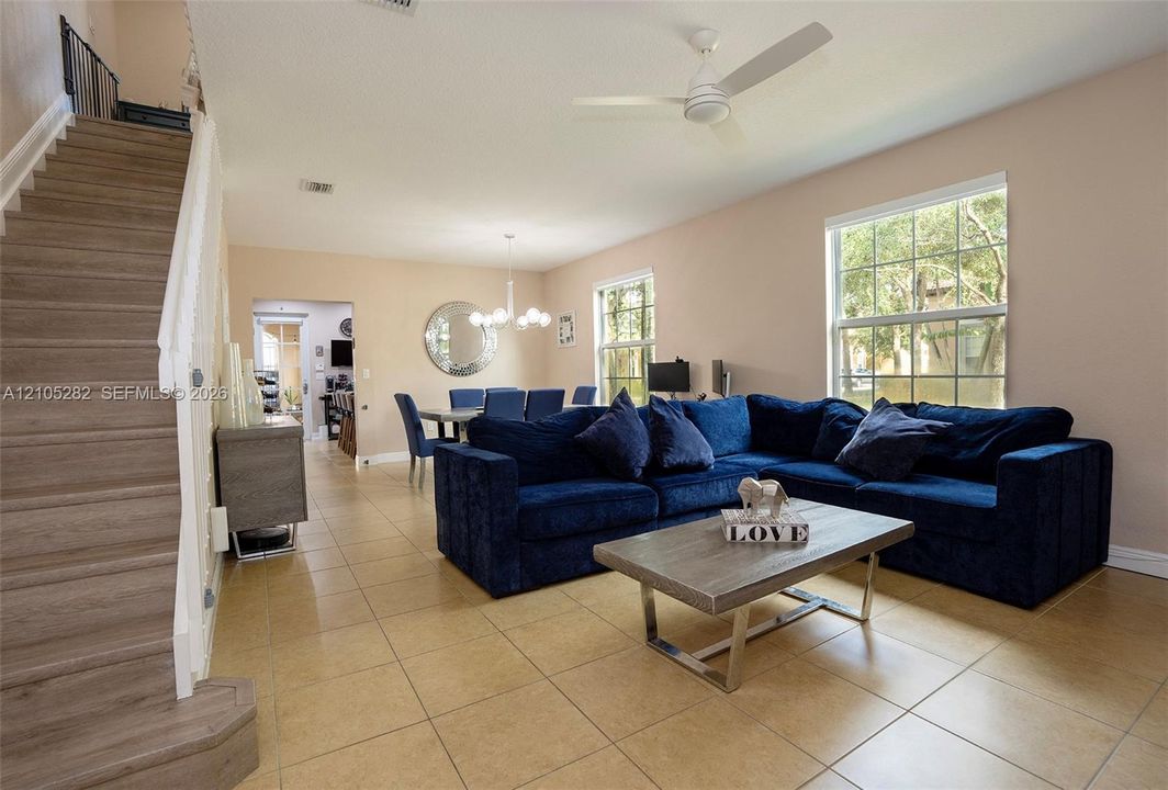 Open-concept interior featuring large-format tile flooring, wood-finish staircase, multi-arm chandelier, and white ceiling-mounted fan