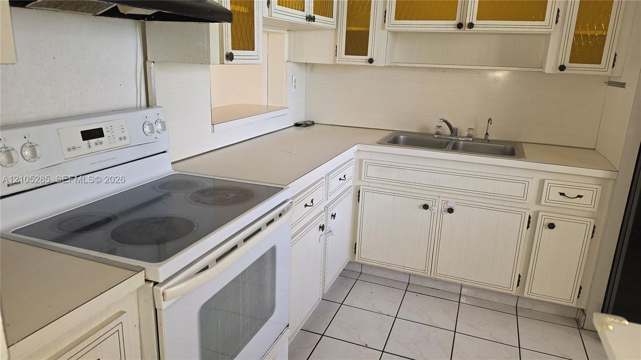 Kitchen featuring white cabinetry, solid-surface countertops, dual-basin stainless steel sink, tile flooring, and a white electric range