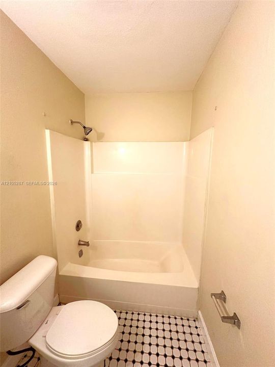 Tub/shower combination with a showerhead, faucet, and textured ceiling