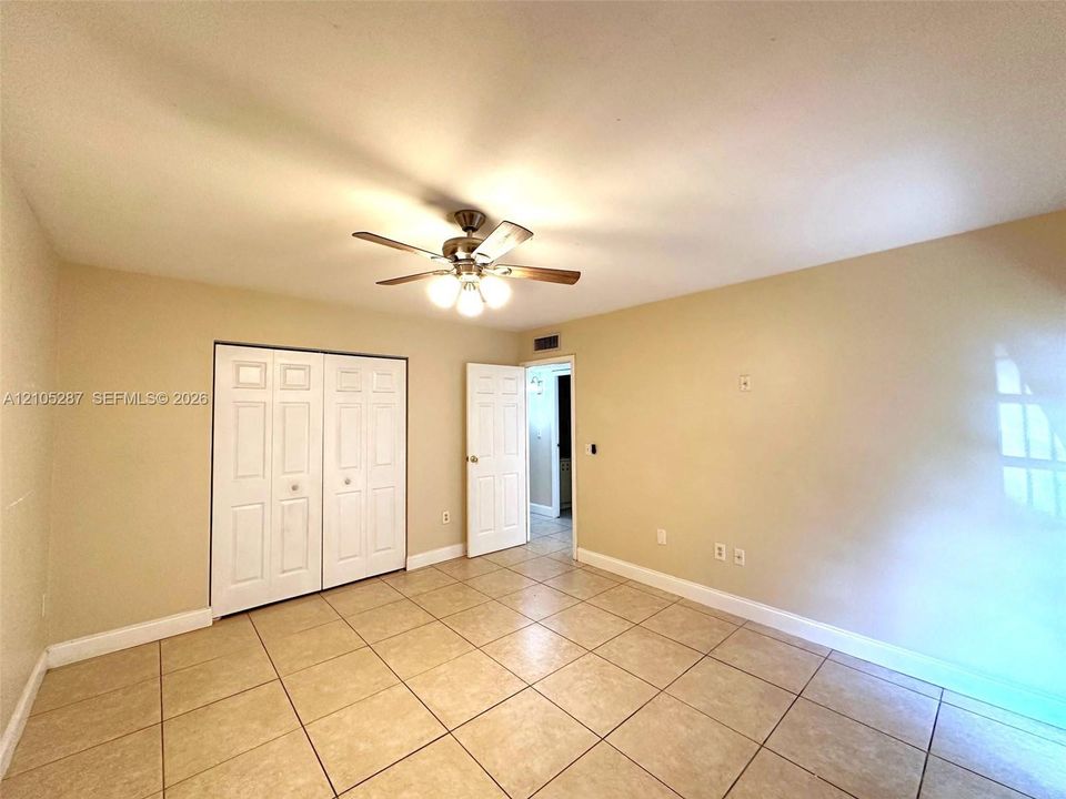 Square tile flooring, bi-fold closet doors, ceiling fan with integrated lighting, and a neutral color palette