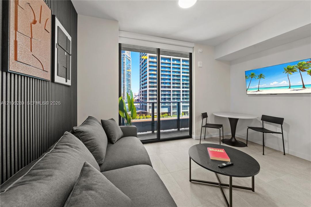 Floor-to-ceiling glass doors, a decorative slat wall accent, a wall-mounted television, a white round pedestal table, and light-toned tile flooring