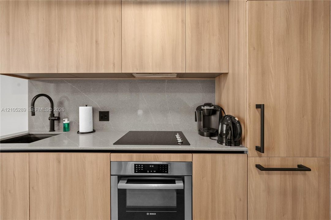 Integrated kitchen with wood-finish cabinetry, black hardware, a flush-mount cooktop, and a stainless-steel built-in oven