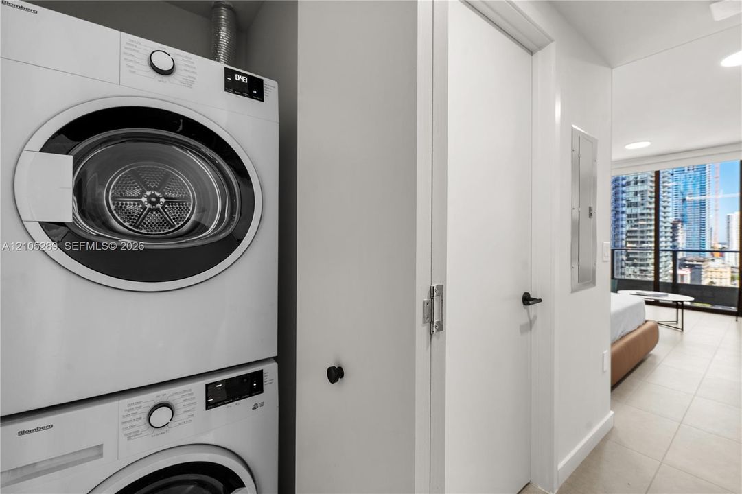Stackable washer and dryer unit, white interior doors with black hardware, and tiled flooring