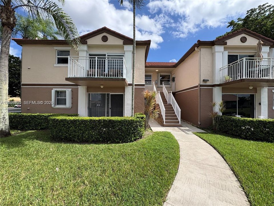 Exterior featuring a stucco finish, tiled roof, multiple private balconies with white railings, and a concrete pathway