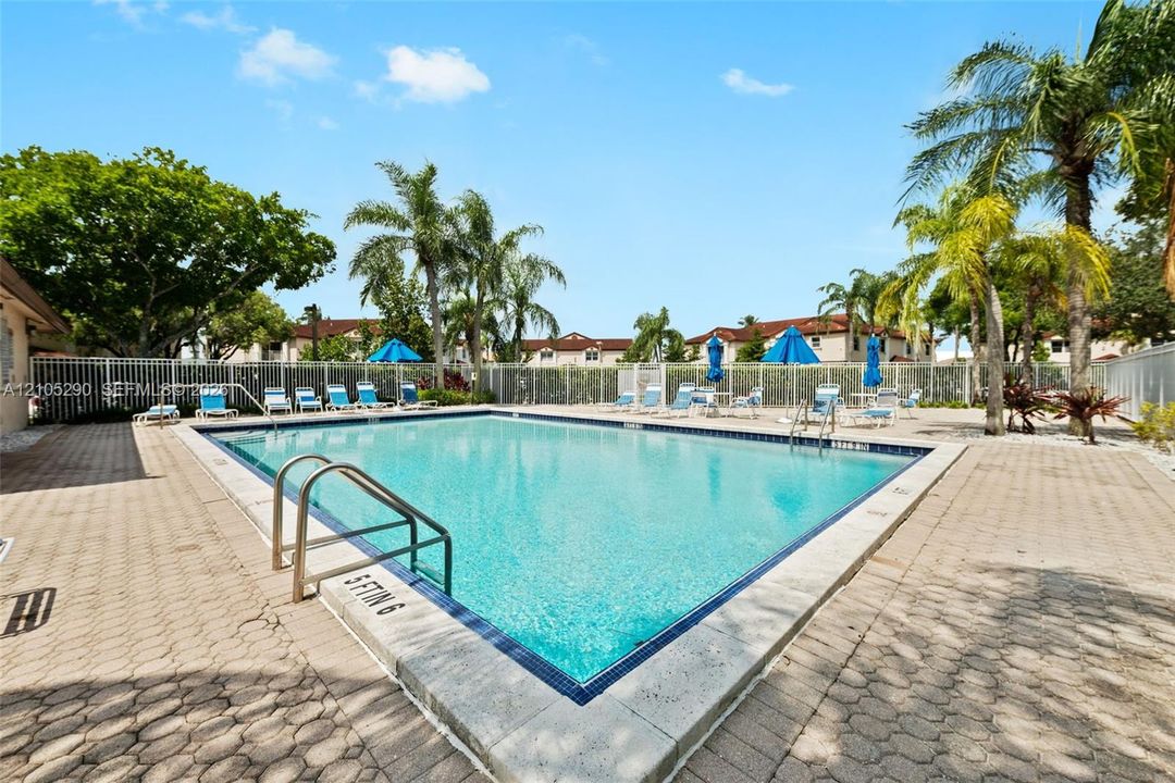 Rectangular swimming pool featuring a tiled waterline, metal grab rails, and surrounding paver decking