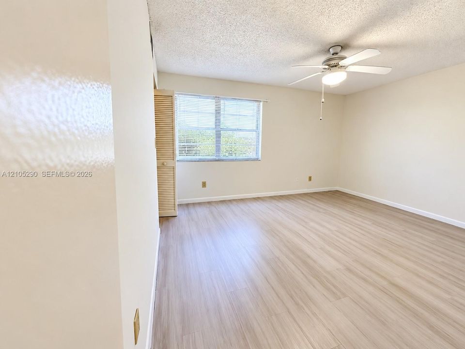 Spacious room featuring wood-finish flooring, a window with blinds, and a ceiling fan with integrated lighting