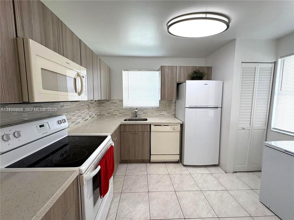 Modern kitchen featuring wood-finish cabinetry, light-toned countertops, and a full suite of appliances