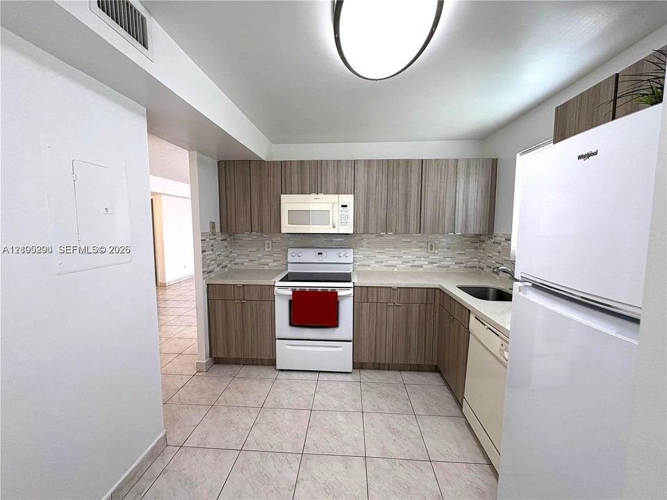 Kitchen featuring wood-finish cabinetry, light-toned countertops, a tile backsplash, white appliances, and tiled flooring