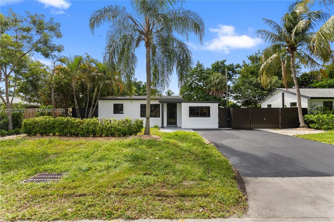 Modern exterior with white siding and dark trim, featuring a dark asphalt driveway, established palm trees, and mature landscaping