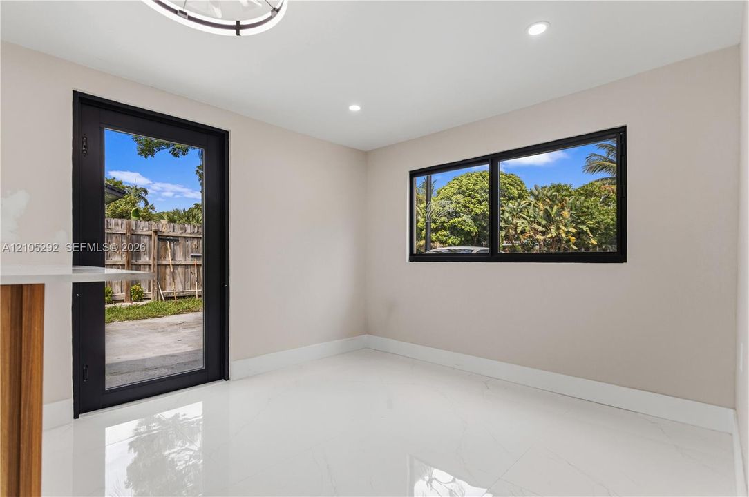 Recessed lighting, wood-finish cabinetry, bright white flooring, black-framed glass door, and black-framed window