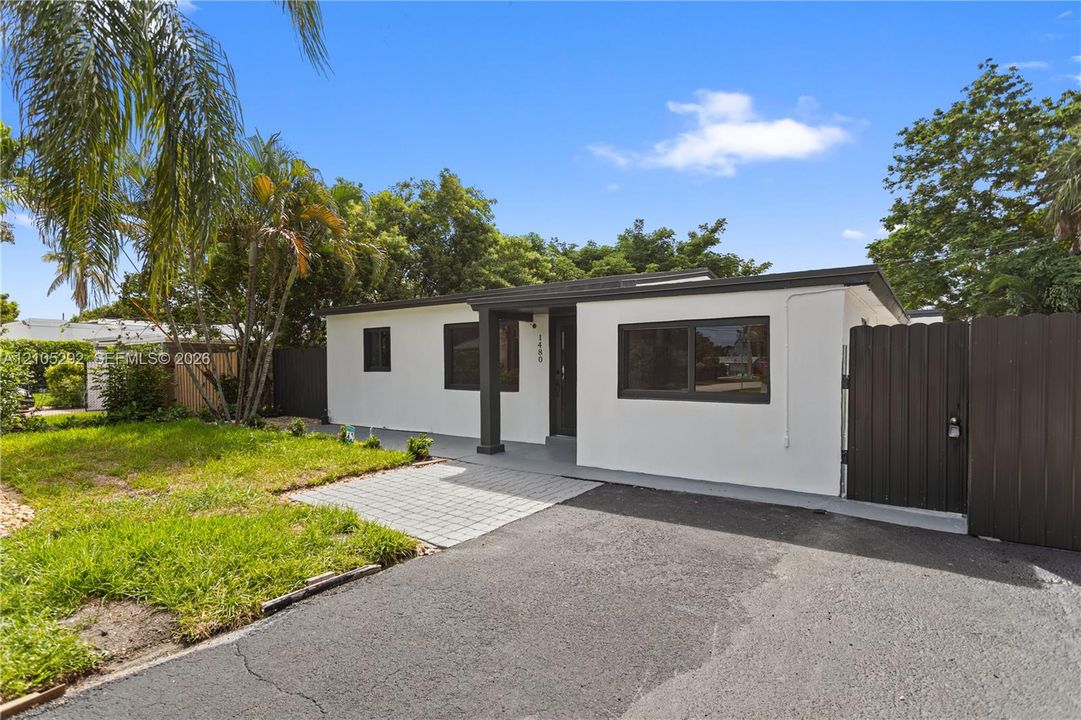 Single-story exterior with white stucco finish, dark trim windows, covered entry, gray paver walkway, and dark privacy fence
