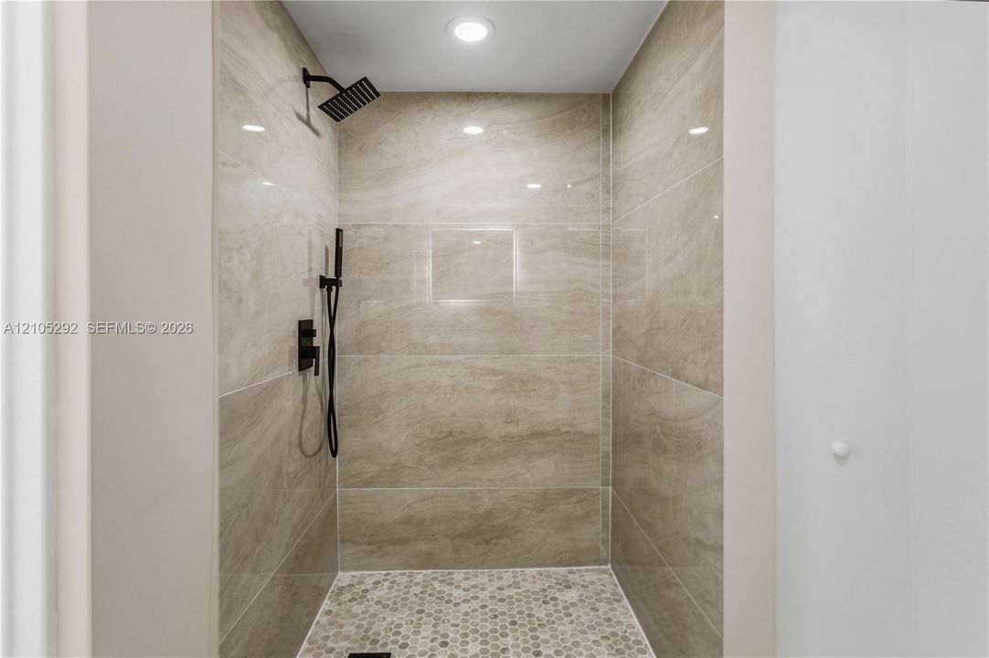 Walk-in shower with large-format wall tiles, hexagonal floor tiles, and matte black shower fixtures