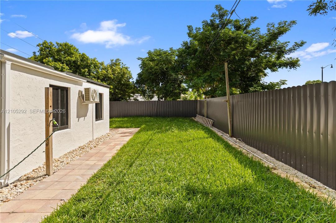 Expansive lawn area, concrete paver pathway, gravel landscaping, stucco exterior, and a solid perimeter fence