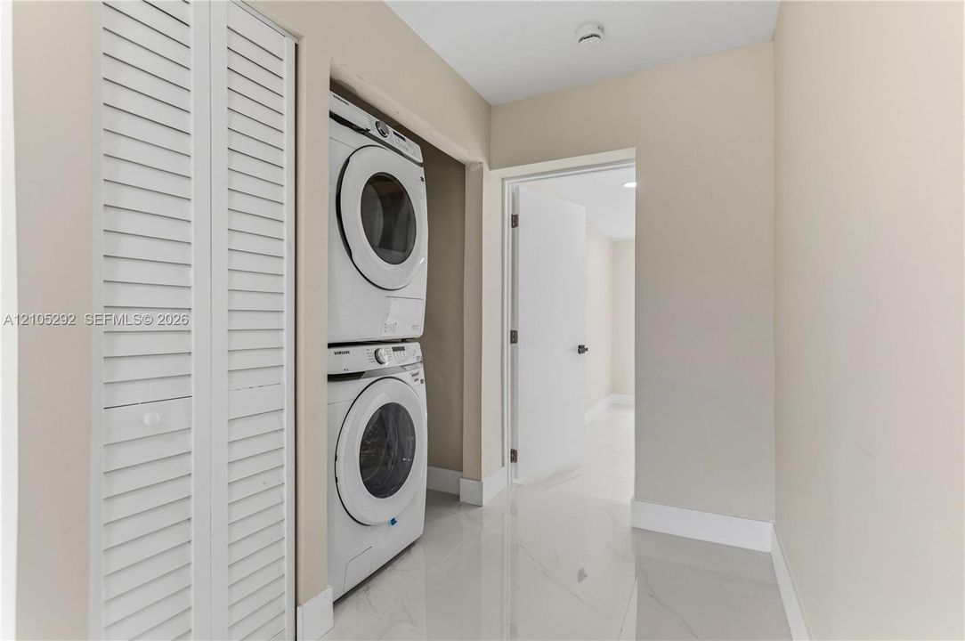Laundry closet featuring a stacked washer and dryer, white louvered bifold doors, and a tiled floor