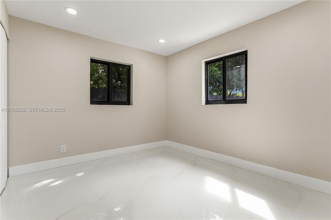 Recessed ceiling lighting, two windows with dark frames, light-toned walls, and white tile flooring