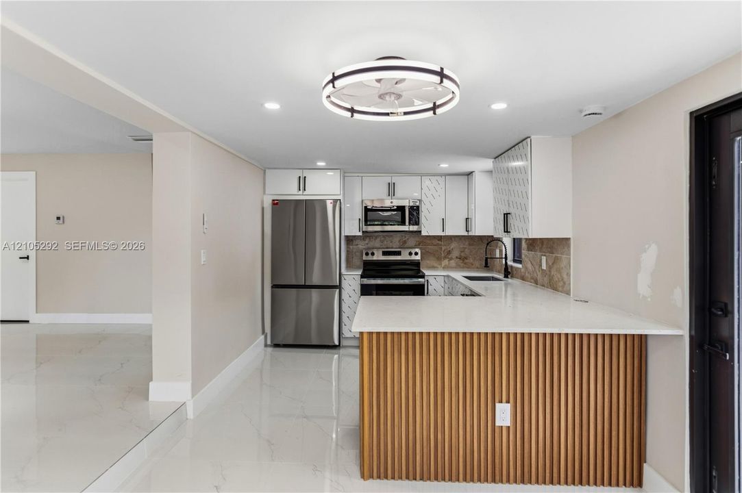 Kitchen with white cabinetry, stainless steel appliances, a tile backsplash, and a breakfast bar with a wood-slat base