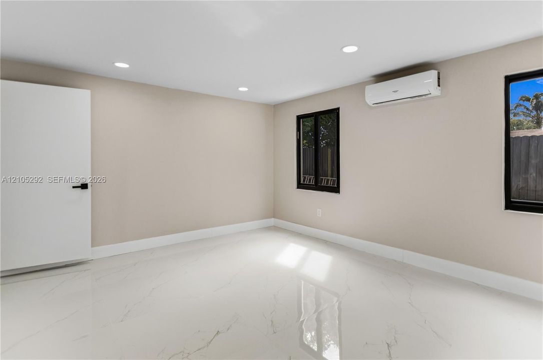 Recessed ceiling lighting, white tile flooring, mini-split air conditioning unit, white interior door with black hardware, and black-framed windows