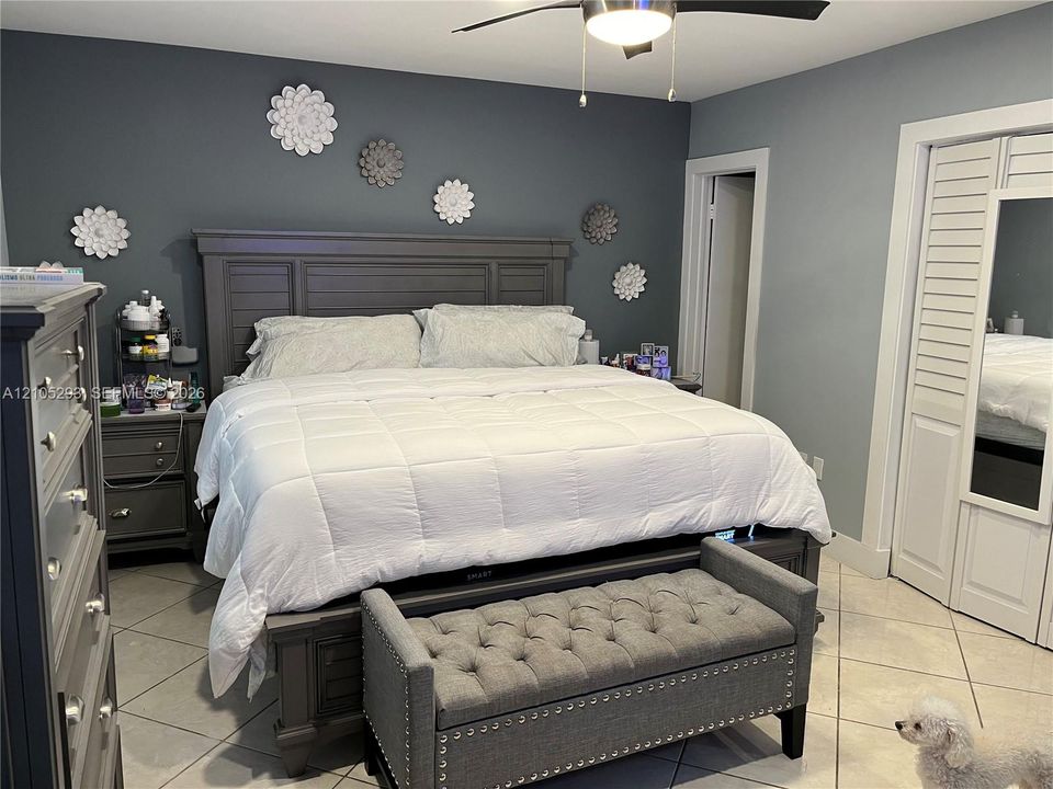 Large-format tile flooring, louvered closet doors with integrated mirror, and a ceiling-mounted light fixture with fan
