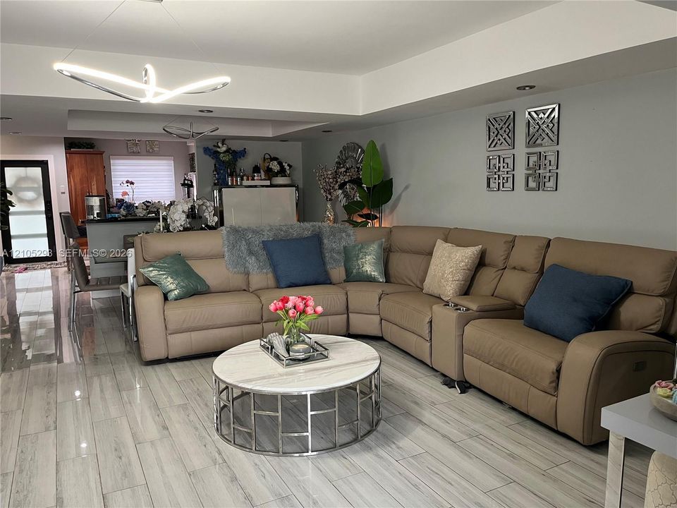Open-concept interior featuring wood-finish tile flooring, recessed ceiling lighting, a modern geometric pendant light fixture, and crown molding