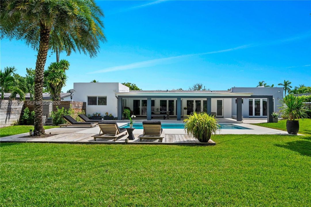 Backyard featuring a swimming pool, covered patio with structural columns, wood-finish decking, and manicured lawn