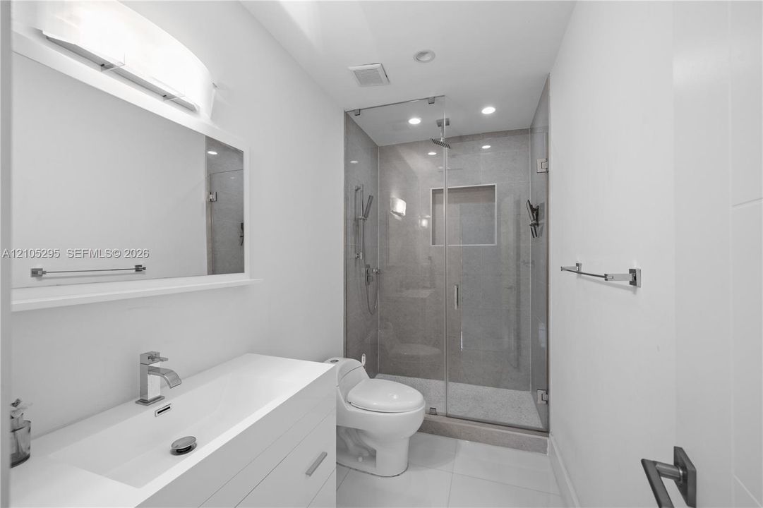 White floating vanity with integrated rectangular sink, chrome widespread faucet, glass-enclosed shower featuring a recessed wall niche, and polished tile flooring