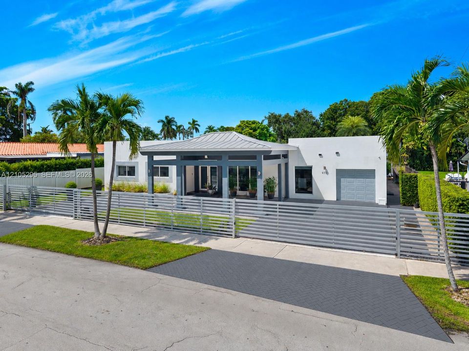 Single-story exterior featuring a metal roof, integrated front porch, paved herringbone driveway, and horizontal privacy fencing