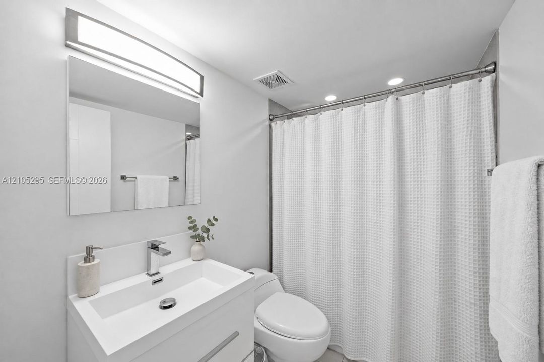 Modern bathroom vanity with a white rectangular basin, polished chrome single-handle faucet, integrated wall-mounted mirror, linear LED vanity light, and a shower-tub combination