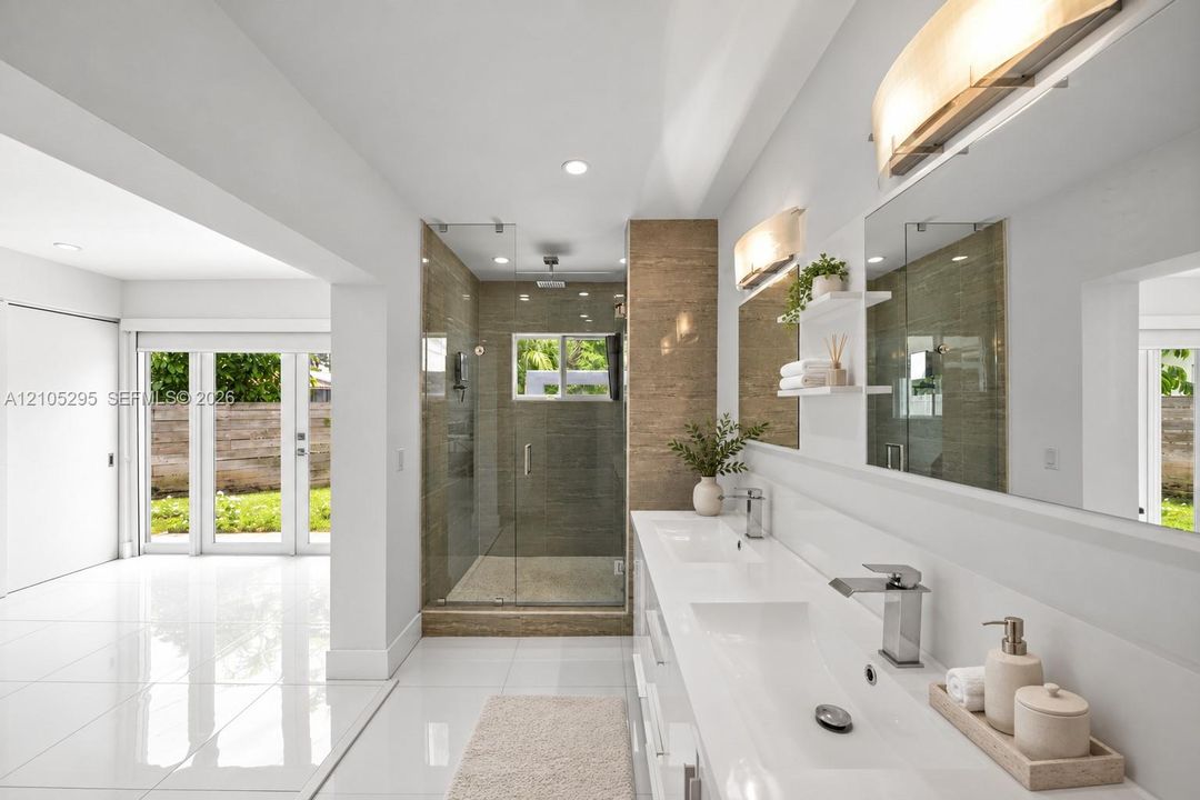 Dual-sink vanity with white countertop, walk-in glass-enclosed shower featuring textured tile surround, polished tile flooring, and integrated wall-mounted lighting