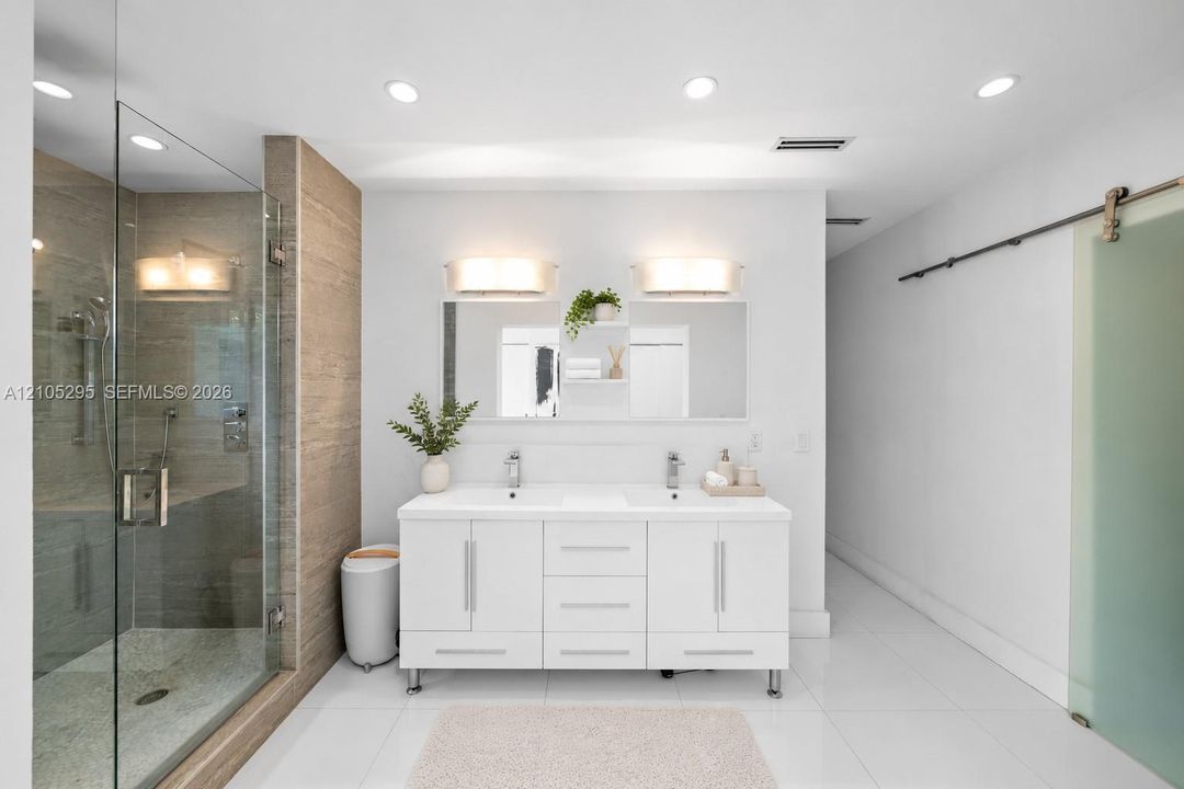 Dual-vanity cabinet with integrated rectangular sinks, walk-in glass-enclosed shower featuring textured tile surround, wall-mounted light fixtures, and sliding frosted glass door